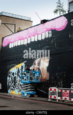 Deux artistes de graffiti - pourrait être le "Burning Candy Crew' - décorer un mur dans la ville de Londres. UK. Banque D'Images