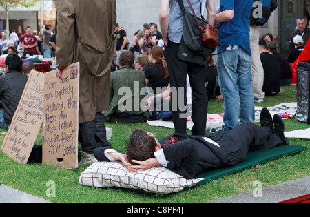 Homme en costume couché à côté de l'homme avec des pancartes écrites à la main au lieu de protestation Perth occupent pour coïncider avec le début d'RCGPC Banque D'Images