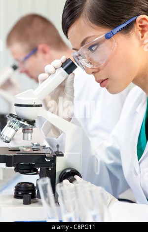 Une femme d'origine asiatique chinois chercheur scientifique ou médical ou un médecin à l'aide d'un microscope dans un laboratoire avec son collègue Banque D'Images