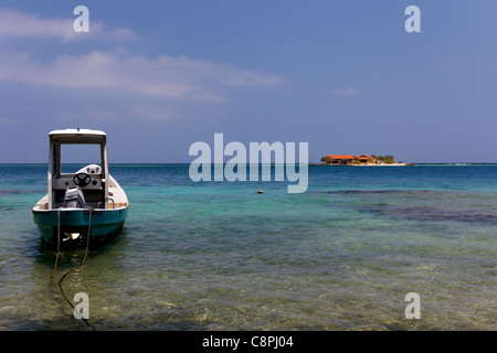 Un petit bateau ancré au premier plan, avec une minuscule île des Caraïbes visible dans l'arrière-plan. Banque D'Images