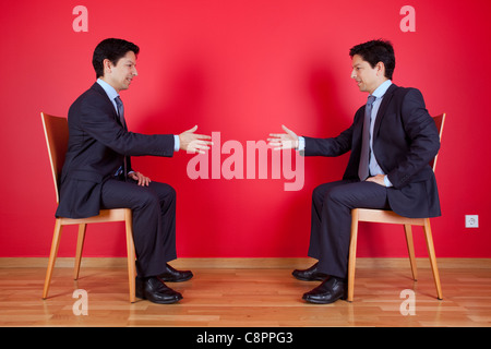 Accord entre l'établissement de deux lits businessman assis sur une chaise à côté d'un mur rouge Banque D'Images