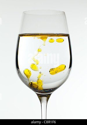 L'huile d'olive est versé dans un grand verre de vin d'or formant des bulles dans le liquide Banque D'Images