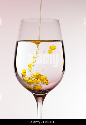 L'huile d'olive est versé dans un grand verre de vin d'or formant des bulles dans le liquide Banque D'Images