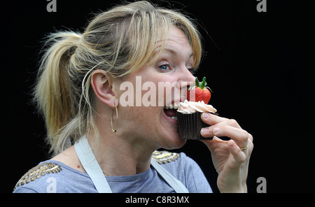 Et le célèbre chef cookbook auteur Rachel Allen illustré de manger un petit gâteau sur un fond noir. Banque D'Images