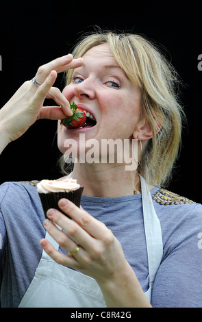 Et le célèbre chef cookbook auteur Rachel Allen illustré de manger un petit gâteau sur un fond noir. Banque D'Images