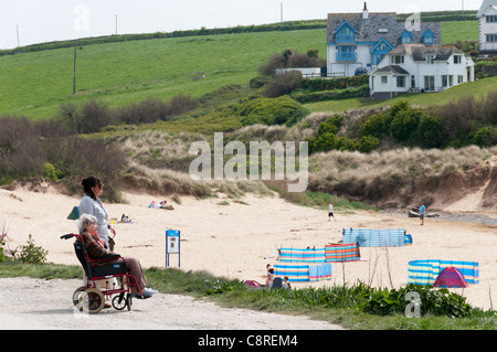 Une femme âgée avec un accompagnant ou assistant sur un chemin accessible en fauteuil roulant derrière une plage de Cornouailles. Parution du modèle. Banque D'Images