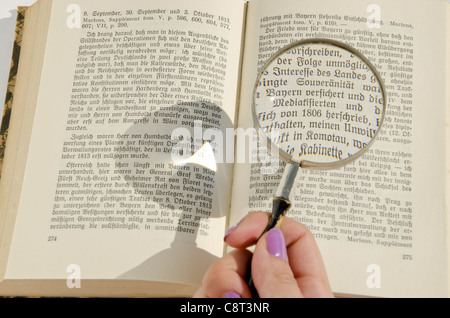 Woman's hand holding loupe sur la page livre allemand. Texte élargie détail. Banque D'Images