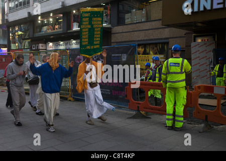 Un déplacement d'ouvriers travaillant dans Leicester Square sont à quelques dévots Hare Krishna qui danse Le chant passé. Banque D'Images