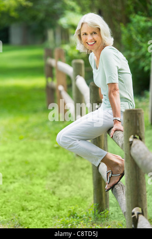 USA, New York State, Old Westbury, Portrait of senior woman sitting on fence Banque D'Images