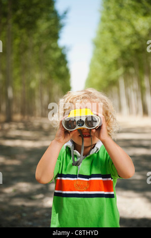 USA, Ohio, Boardman, Boy looking through binoculars in tree farm Banque D'Images