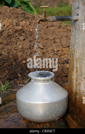 L'eau potable à partir de la borne fontaine en cascade dans une casserole en aluminium sur une rive du fleuve sur les Backwaters du Kerala, Inde Banque D'Images