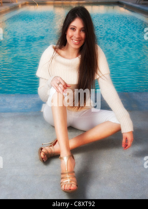 Young Hispanic woman 20s'assoit au bord de l'après-midi le port de chandail beige / blanc luxueux, pantalons capri heels Banque D'Images