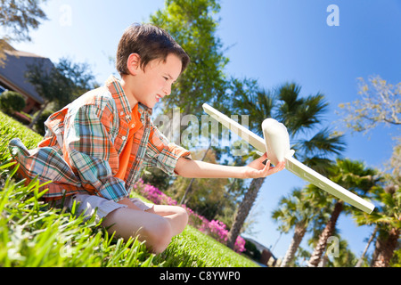 Un jeune garçon assis sur l'herbe à l'extérieur à jouer avec un jouet maquette avion