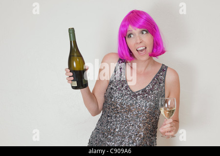 Funny photo de Caucasian woman wearing party rose vif perruque et robe, boire du vin mousseux Banque D'Images