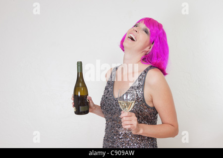 Funny photo de Caucasian woman wearing party rose vif perruque et robe, boire du vin mousseux Banque D'Images