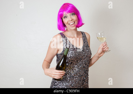 Funny photo de Caucasian woman wearing party rose vif perruque et robe, boire du vin mousseux Banque D'Images