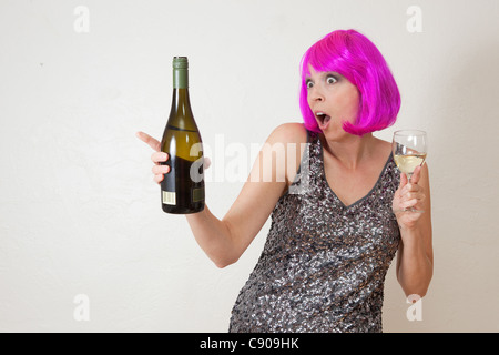 Funny photo de Caucasian woman wearing party rose vif perruque et robe, boire du vin mousseux Banque D'Images