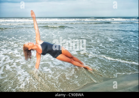 Jeune femme la trentaine cheveux mouillés effectue la position de Yoga dans l'eau à la mer noire de l'océan l'un veston beige Vue de côté des membres sains Banque D'Images
