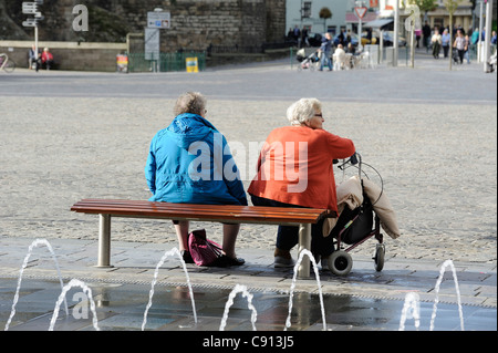 Deux vieilles dames assises sur un banc dans le square caernarfon avec les fontaines dansantes dans l'avant-plan gwynedd au nord du Pays de Galles UK Banque D'Images