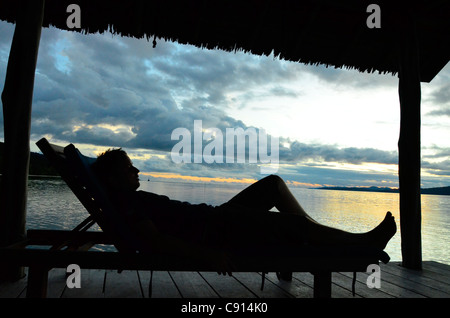 'Allongé sur le dos au coucher du soleil sur l'embarcadère de Kri Eco Resort, Raja Ampat îles de Papouasie occidentale dans l'océan Pacifique, l'Indonésie. Banque D'Images
