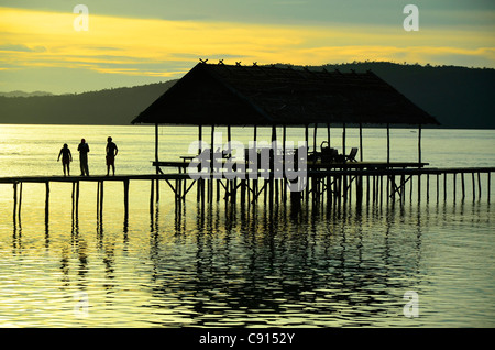 Trois touristes marcher sur pierre au coucher du soleil, Kri Eco Resort, Raja Ampat îles de Papouasie occidentale dans l'océan Pacifique, l'Indonésie. Banque D'Images