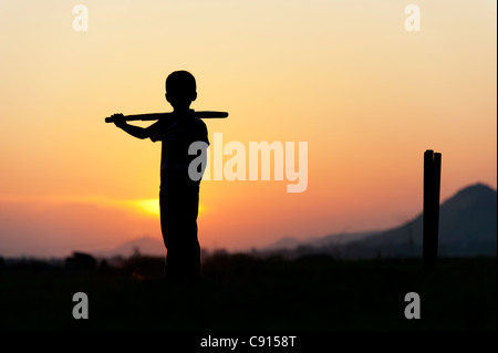 Silhouette de jeune garçon indien à jouer au cricket contre un fond coucher de soleil Banque D'Images