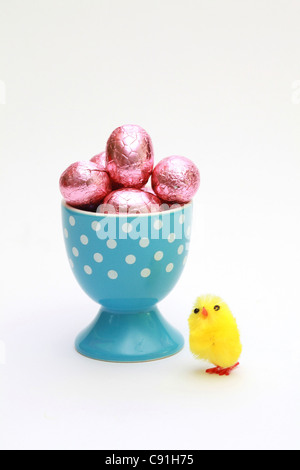 Un peu faux poulet à côté d'un coquetier rempli d'oeufs en chocolat de Pâques Banque D'Images