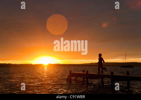 Boy running on wooden dock au coucher du soleil Banque D'Images