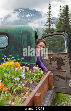 Une jeune femme Inupiat inspecte l'intérieur d'un vieux camion transformé en un lit de fleur à Crow Creek près de Girdwood, Alaska Banque D'Images