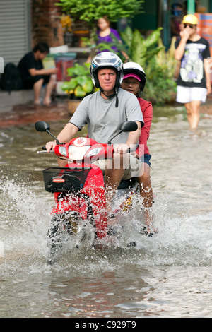 Couple riding a moto à travers l'eau d'inondation en centre-ville de Bangkok, Thaïlande Banque D'Images