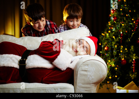 Photo de Père Noël dormir sur un canapé avec deux garçons heureux de le regarder Banque D'Images