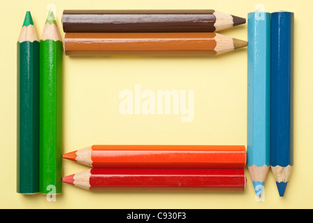 Colorful crayons de couleur formant un rectangle cadre sur un morceau de papier jaune Banque D'Images