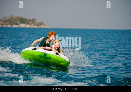 Au Malawi, le lac Malawi National Park. Deux jeunes garçons monter sur un anneau gonflable tiré par un hors-bord. M. Banque D'Images