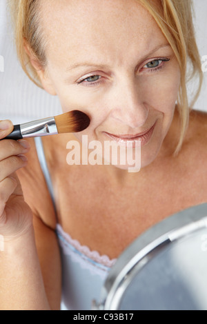 Mid age woman putting on make-up Banque D'Images