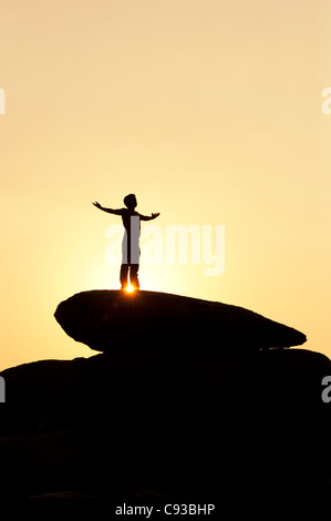 Homme debout sur un rocher qui englobe le soleil. Silhouette. L'Inde Banque D'Images