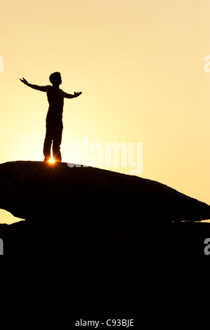 Homme debout sur un rocher qui englobe le soleil. Silhouette. L'Inde Banque D'Images