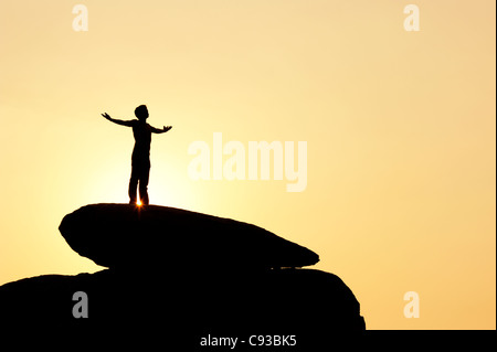 Homme debout sur un rocher qui englobe le soleil. Silhouette. L'Inde Banque D'Images