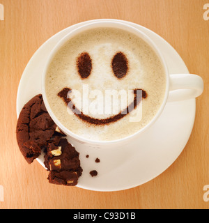 Cappuccino avec smiley face dans le chocolat en poudre et d'un cookie sur la soucoupe. Banque D'Images