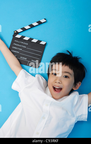 Garçon avec clapper board couchée sur le plancher, studio shot Banque D'Images