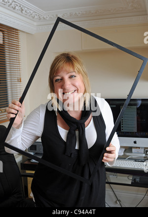 Woman working in office looking through empty picture frame smiling Photo prise Novembre 2011 Banque D'Images