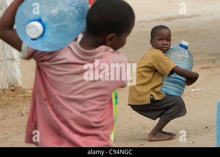 Les enfants transportent l'eau de l'arrière d'un puits à Dar es Salaam, Tanzanie, Afrique de l'Est. Banque D'Images