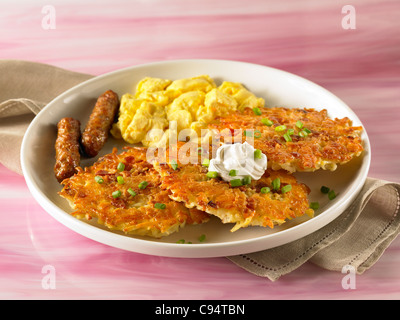 Petit déjeuner aux crêpes de pommes de terre garnies de crème aigre et servi avec des œufs brouillés et des saucisses Banque D'Images