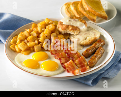 Un petit-déjeuner pays d'alimentation avec trois oeufs, bacon, saucisses, petits gâteaux et Sauce, pommes de terre et de pain grillé Banque D'Images