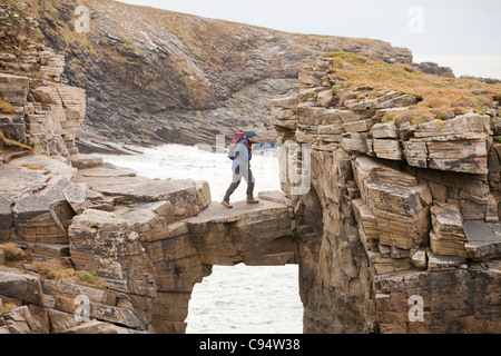 L'alpiniste traverse un pont de pierre cale qui relie les falaises d'une pile de la mer à Yesnaby sur la côte ouest des Orcades Banque D'Images