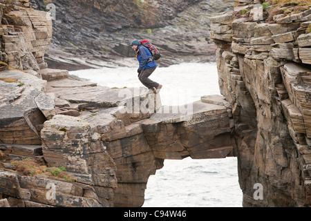 L'alpiniste traverse un pont de pierre cale qui relie les falaises d'une pile de la mer à Yesnaby sur la côte ouest des Orcades Banque D'Images