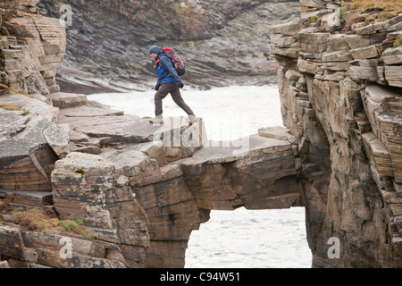 L'alpiniste traverse un pont de pierre cale qui relie les falaises d'une pile de la mer à Yesnaby sur la côte ouest des Orcades Banque D'Images