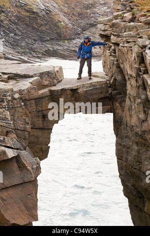 L'alpiniste traverse un pont de pierre cale qui relie les falaises d'une pile de la mer à Yesnaby sur la côte ouest des Orcades Banque D'Images