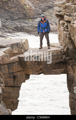 L'alpiniste traverse un pont de pierre cale qui relie les falaises d'une pile de la mer à Yesnaby sur la côte ouest des Orcades Banque D'Images