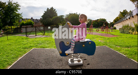 Un petit enfant dans une robe rose monté sur un cheval à bascule dans une aire de jeux. Banque D'Images