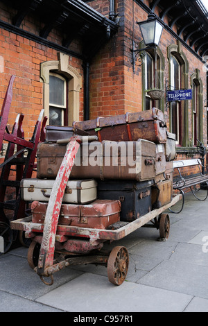 De vieilles valises empilées sur un chariot à une gare recréant une scène de voyage communément vue dans les années 1940, 1950 et 1960 Banque D'Images